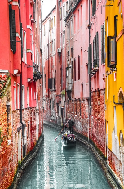 穿黑夹克的人在河上骑着小船在红色和黄色的混凝土建筑物之间穿行